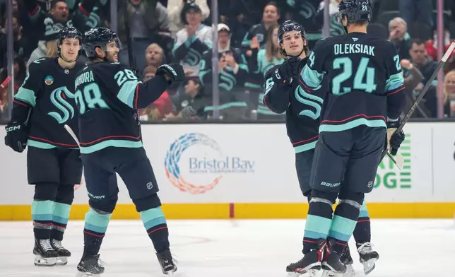 Seattle Kraken defenseman Jamie Oleksiak (24) celebrates with center Ryan Winterton, second right, defenseman Joshua Mahura and left wing Tye Kartye, left, after scoring during the second period of an NHL hockey game against the Chicago Blackhawks Monday, Nov. 3, 2025, in Seattle. (AP Photo/Jason Redmond)