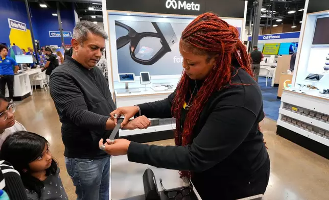Aamir Ghulamani of Carrollton, Texas, gets help from Sydney Rogers, a Meta specialist at Best Buy as Ghulamani samples the glasses, Wednesday, Nov. 26, 2025, in Dallas. (AP Photo/Tony Gutierrez)