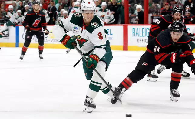 Minnesota Wild's Zeev Buium (8) tries to backhand a shot around Carolina Hurricanes' Joel Nystrom (64) during the first period of an NHL hockey game in Raleigh, N.C., Thursday, Nov. 6, 2025. (AP Photo/Karl DeBlaker)