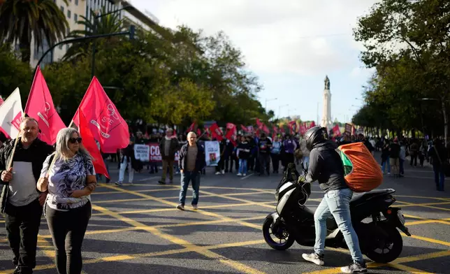 A delivery rider pushes his bike to cross the path of demonstrators marching down Lisbon's Liberdade Avenue during a national protest by workers unions against a new labour package being prepared by the government, Saturday, Nov. 8, 2025. (AP Photo/Armando Franca)