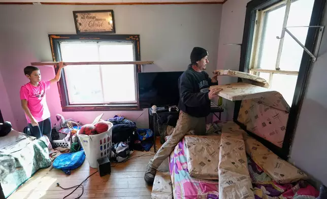 Gerard Berry covers a broken window with insulation before he and his son, Aidan, tape plastic over the windows, Friday, Nov. 7, 2025, in Baileyville, Maine. (AP Photo/Robert F. Bukaty)