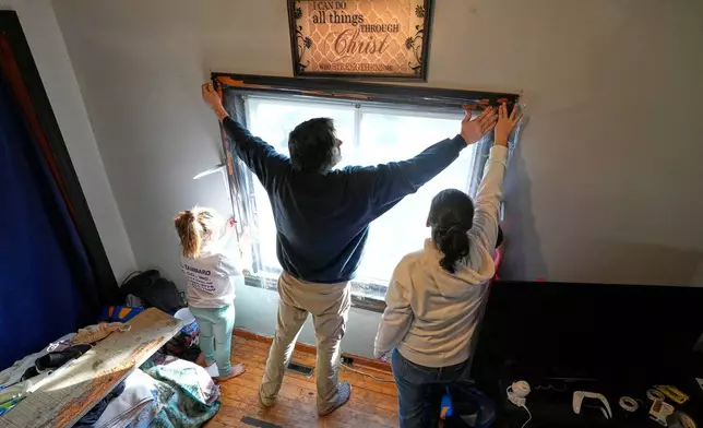 Gerard Berry, along with his wife, Stephanie, and daughter, Brooklynn, cover a bedroom window with plastic, Friday, Nov. 7, 2025, in Baileyville, Maine. (AP Photo/Robert F. Bukaty)