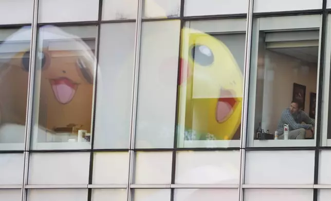 People inside office buildings watch as the Pikachu balloon passes during the Macy's Thanksgiving Day Parade, Thursday, Nov. 27, 2025, in New York. (AP Photo/Heather Khalifa)
