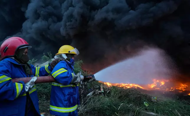 Female firefighter Syeda Masooma Zaidi, right, with her team member spray water to extinguish on a fire broke out in a storage facility packed vehicles tires, outskirts of Karachi, Pakistan, Thursday, Oct. 30, 2025. (AP Photo/Fareed Khan)
