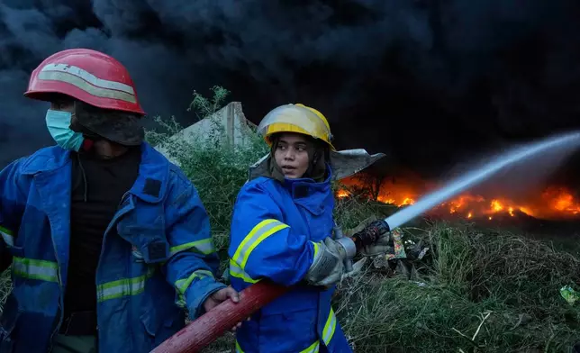 **EDITORS NOTE: ADVANCE PHOTO ISL501-516, PLEASE HOLD THEM FOR THE RELEASE OF A FEATURE STORY SLUG: 'PAKISTAN WOMEN FIREFIGHTERS' BY MUNIR AHMED ** Female firefighter Syeda Masooma Zaidi, right, with her team member spray water to extinguish on a fire broke out in a storage facility packed vehicles tires, outskirts of Karachi, Pakistan, Thursday, Oct. 30, 2025. (AP Photo/Fareed Khan)