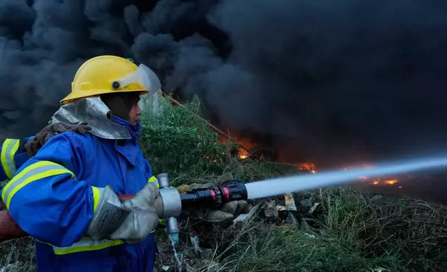 Female firefighter Syeda Masooma Zaidi sprays water to extinguish on a fire broke out in a storage facility packed vehicles tires, outskirts of Karachi, Pakistan, Thursday, Oct. 30, 2025. (AP Photo/Fareed Khan)