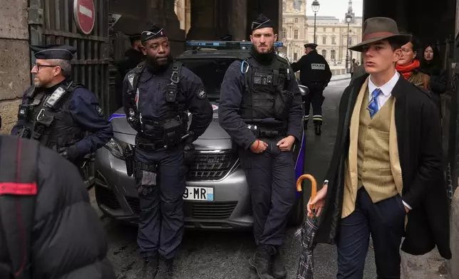 FILE - Pedro Elias Garzon Delvaux, right, walks past as police officers block an entrance to the Louvre after thieves carried out a daylight raid on French crown jewels, in Paris, Oct. 19, 2025. (AP Photo/Thibault Camus, File)