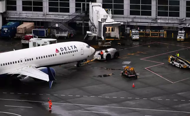 A ground crew worker signals a plane next to a Delta Airlines aircraft at Seattle-Tacoma International Airport, Thursday, Nov. 6, 2025, in SeaTac, Wash. (AP Photo/Lindsey Wasson)