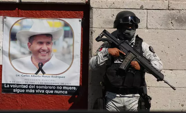 A National Guards stands guard next to a portrait of slain Mayor Carlos Manzo Rodriguez in Uruapan, Mexico, as Michoacan state prosecutors detain suspects in the investigation into his killing, Friday, Nov. 21, 2025. (AP Photo/Eduardo Verdugo)