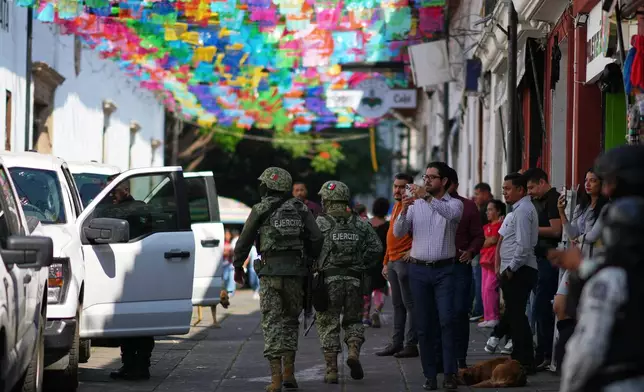 Soldiers patrol and pedestrians watch as Michoacan state prosecutor officers escort a suspect in the killing of the town's Mayor Carlos Manzo Rodriguez in Uruapan, Mexico, Friday, Nov. 21, 2025. (AP Photo/Eduardo Verdugo)