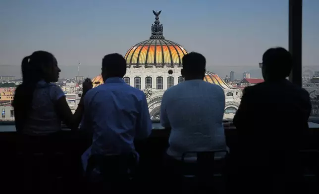 People sit at a rooftop bar overlooking Mexico City's Fine Arts Palace, where the Mexican coat of arms is visible atop the building's dome, Thursday, Nov. 13, 2025. (AP Photo/Claudia Rosel)