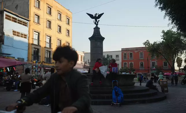 People at the square of Aguilita in Mexico City walk past a central sculpture depicting Mexico's coat of arms which shows an eagle perched on a cactus devouring a rattlesnake, Thursday, Nov. 13, 2025. (AP Photo/Claudia Rosel)