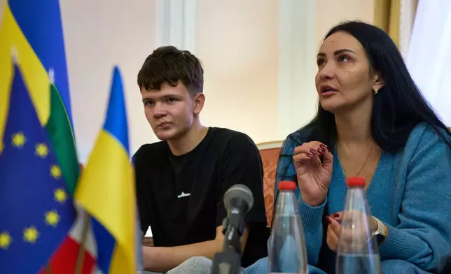 Mark Razvozov, left, listens to his mother Yukiia Dvornychenko, during a press conference on the return of Ukrainian children and civilians taken by Russia during the three-and-a-half-year war, at the Embassy of Ukraine in Italy, in Rome, Wednesday, Nov. 19, 2025. (AP Photo/Domenico Stinellis)