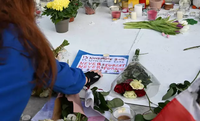 A woman touches a message at the statue of the Place de la Republique (Republic Square) as Paris is marking the 10th anniversary of terrorist attacks that killed 132 people and injured hundreds, Thursday, Nov. 13, 2025 in Paris. (AP Photo/Emma Da Silva)