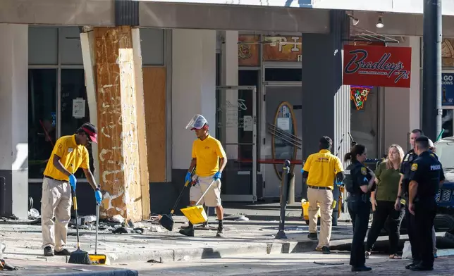 People clean up the damage from a car that crashed into a local business, while law enforcement investigate the scene on Saturday, Nov. 8, 2025, in Tampa, Fla. (Jefferee Woo/Tampa Bay Times via AP)