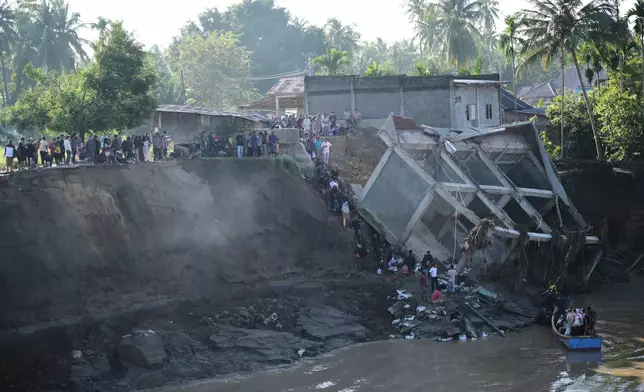 People walk down the embankment of a river to take a boat ride across after a bridge nearby collapsed during a flood in Bireun, Aceh province, Indonesia, Saturday, Nov. 29, 2025. (AP Photo/Reza Saifullah)