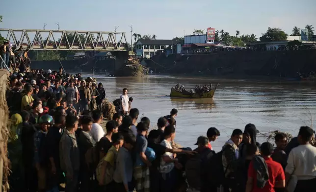 People wait for a boat to ride across a river after a bridge nearby collapsed during a flood in Bireun, Aceh province, Indonesia, Saturday, Nov. 29, 2025. (AP Photo/Reza Saifullah)