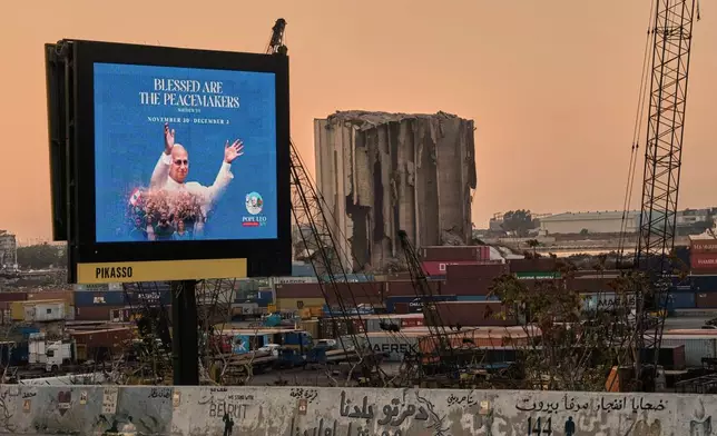 A billboard displays an image of Pope Leo XIV, ahead of his upcoming visit to Lebanon, near the grain silos at Beirut's port that were heavily damaged in the massive 2020 explosion as a graffiti in Arabic reading "Victims of the Beirut port explosion" is seen in the foreground, Thursday, Nov. 20, 2025. (AP Photo/Hassan Ammar)