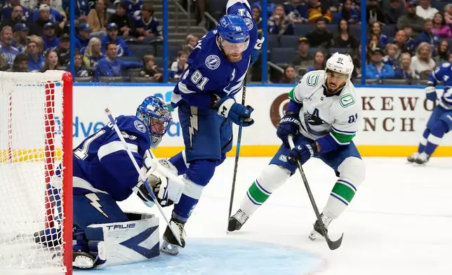 Tampa Bay Lightning defenseman Erik Cernak (81) and Vancouver Canucks left wing Evander Kane (91) chase a loose puck in front of goaltender Jonas Johansson (31) during the first period of an NHL hockey game Sunday, Nov. 16, 2025, in Tampa, Fla. (AP Photo/Chris O'Meara)