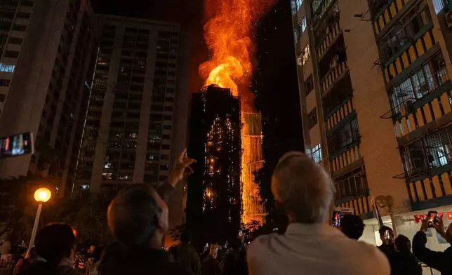 People look at flames engulfing a building after a fire broke out at Wang Fuk Court, a residential estate in the Tai Po district of Hong Kong's New Territories, Wednesday, Nov. 26 2025. (AP Photo/Chan Long Hei)
