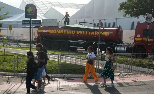 People walk past as a firefighter works at the COP30 U.N. Climate Summit following a fire, Thursday, Nov. 20, 2025, in Belem, Brazil. (AP Photo/Fernando Llano)