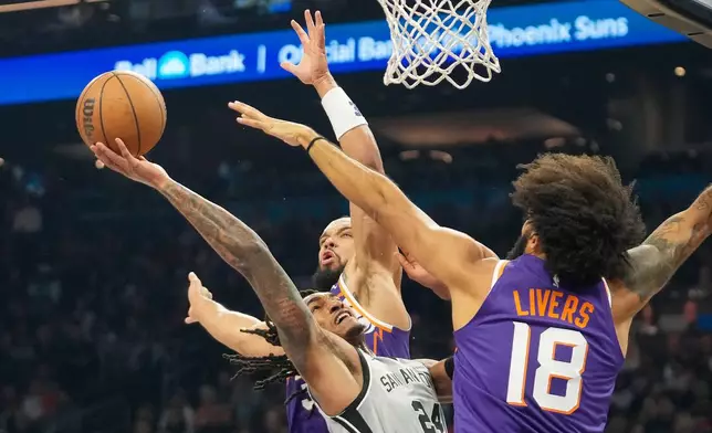 San Antonio Spurs guard Devin Vassell, middle, attempts to shoot between Phoenix Suns forward Dillon Brooks, top, and Isaiah Livers, right, during the first half of an NBA basketball game in Phoenix, Sunday, Nov. 23, 2025. (AP Photo/Darryl Webb)