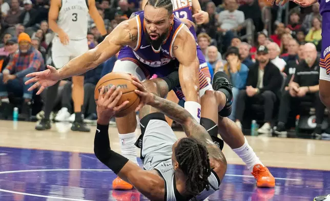 Phoenix Suns forward Dillon Brooks, top, goes for a loose ball against San Antonio Spurs guard Devin Vassell, bottom, during the first half of an NBA basketball game in Phoenix, Sunday, Nov. 23, 2025. (AP Photo/Darryl Webb)