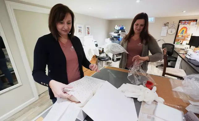 Fran Poirier, left, and her sister, Sue Bacarro, right, fill orders at their Etsy shop Digi Wildflowers, Thursday, Oct. 30, 2025, in Windsor, Ontario, Canada. (AP Photo/Paul Sancya)