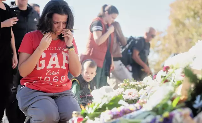 A woman cries before lighting a candle by floral tributes outside the train station on the first anniversary of the disaster that killed 16 people, in Novi Sad, Serbia, Saturday, Nov. 1, 2025. (AP Photo/Armin Durgut)