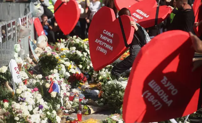 People place heart shaped banners carrying the names of the victims next to floral tributes outside the train station on the first anniversary of the disaster that killed 16 people, in Novi Sad, Serbia, Saturday, Nov. 1, 2025. (AP Photo/Armin Durgut)