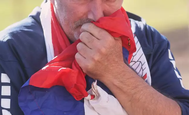 A man clutches a Serbian outside the train station on the first anniversary of the disaster that killed 16 people, in Novi Sad, Serbia, Saturday, Nov. 1, 2025. (AP Photo/Armin Durgut)