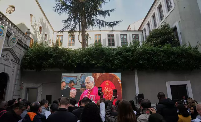 People watch Pope Leo XIV on a screen as he meets the clergy at the Cathedral of the Holy Spirit, in Istanbul, Turkey, Friday, Nov. 28, 2025. (AP Photo/Domenico Stinellis)