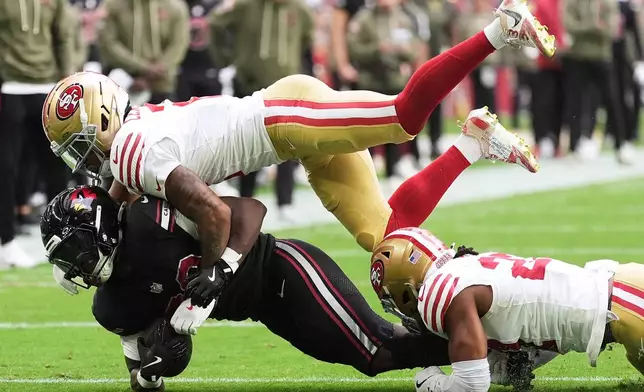 Arizona Cardinals running back Michael Carter, bottom, is tackled by San Francisco 49ers cornerback Deommodore Lenoir, top, and safety Ji'Ayir Brown during the first half of an NFL football game in Glendale, Ariz., Sunday, Nov. 16, 2025. (AP Photo/Ross D. Franklin)