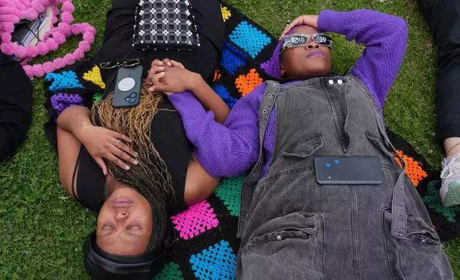 Participants hold hands as they lie on the ground during a gender-based violence protest at the forecourt of the botanical gardens in Johannesburg, South Africa, Friday, Nov. 21, 2025. (Misper Apawu)