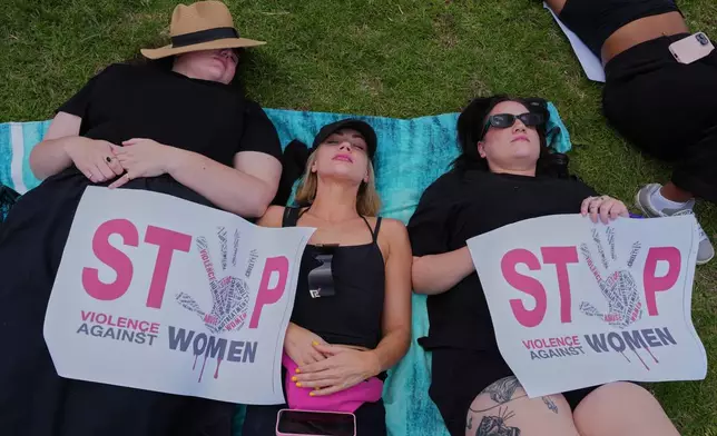 Participants lie on the ground holding signs that read "Stop violence against women" during a gender-based violence protest at the forecourt of the botanical gardens in Johannesburg, South Africa, Friday, Nov. 21, 2025. (Misper Apawu)