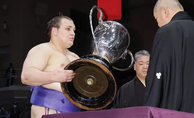 Ukrainian Aonishiki, left, receives the championship trophy after winning the Kyushu Grand Sumo Tournament in Fukuoka, western Japan, Sunday, Nov. 23, 2025. (Kyodo News via AP)