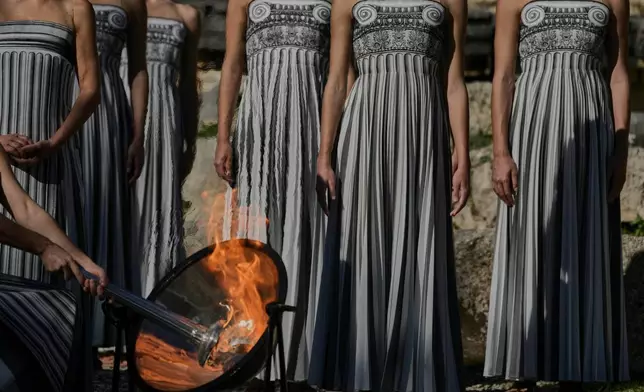 Actress Mary Mina, playing a priestess, lights the flame during a rehearsal ahead of the flame lighting for the Milan Cortina 2026 Winter Olympics, at the Ancient Olympia site, Greece, Monday, Nov. 24, 2025. (AP Photo/Petros Giannakouris)