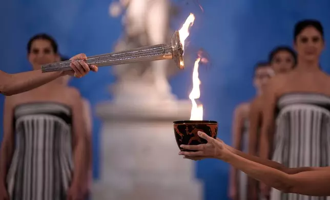 High Priestess Mary Mina, left, lights a torch from the Olympic flame during the flame lighting ceremony for the Milan Cortina 2026 Winter Olympics, at the archaeological museum of Olympia, Greece, Wednesday, Nov. 26, 2025. (AP Photo/Thanassis Stavrakis)