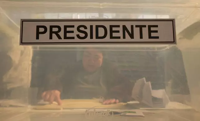 An electoral worker sits behind the ballot box at a polling station during general elections in Santiago, Chile, Sunday, Nov. 16, 2025. (AP Photo/Esteban Felix)