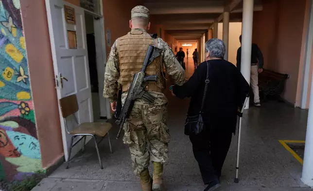 A soldier walks with a voter inside a polling station during general elections in Santiago, Chile, Sunday, Nov. 16, 2025. (AP Photo/Esteban Felix)