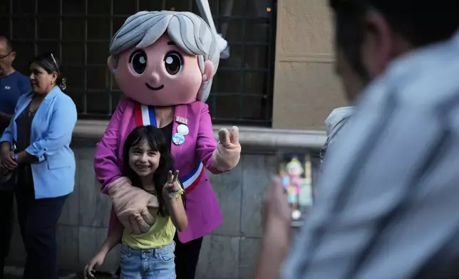 A child poses with a person dressed up as presidential candidate Jeannette Jara of the Unidad por Chile coalition after the polls closed during general elections in Santiago, Chile, Sunday, Nov. 16, 2025. (AP Photo/Natacha Pisarenko)