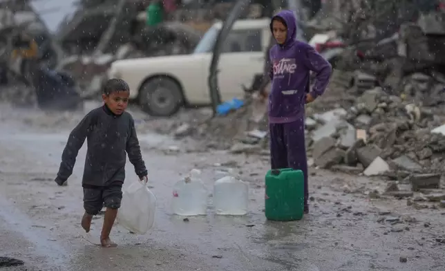 A barefoot boy walks in the rain carrying a plastic jerrycan of water in the Sheikh Radwan neighborhood of Gaza City, Friday, Nov. 14, 2025. (AP Photo/Jehad Alshrafi)