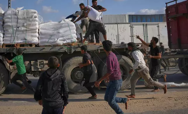 Palestinians grab sacks of flour from a moving truck carrying World Food Programme (WFP) aid as it drives through Deir al-Balah in central Gaza, Saturday, Nov. 15, 2025. (AP Photo/Abdel Kareem Hana)