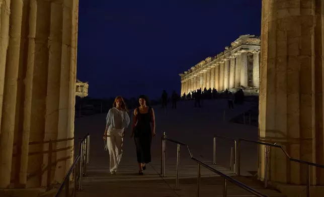 Tourists walk in front of the illuminated 5th century B.C. Parthenon atop the Acropolis hill in Athens, Friday, Oct. 31, 2025. (AP Photo/Petros Giannakouris)