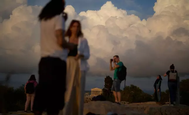 Tourists stand on Filopappos Hill with the ancient Parthenon atop the Acropolis in the background, in Athens, Tuesday, Oct. 21, 2025. (AP Photo/Petros Giannakouris)