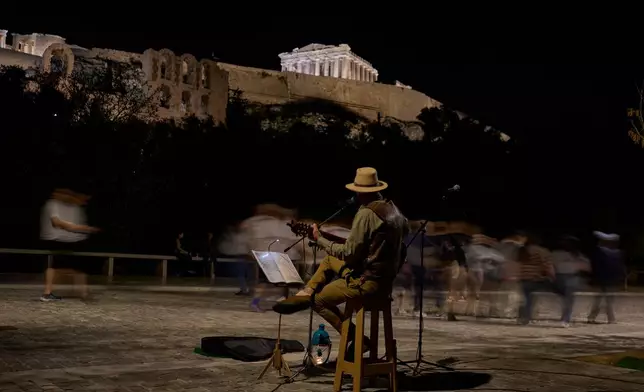 Street musician Marinos Kyriakopoulos performs as pedestrians walk by in front of the Parthenon temple atop the Acropolis hill, in Athens, Tuesday Oct. 28, 2025. (AP Photo/Petros Giannakouris)