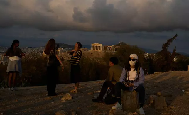 Tourists stand on Filopappos Hill with the ancient Parthenon temple atop the Acropolis hill in the background, in Athens, Tuesday, Oct. 21, 2025. (AP Photo/Petros Giannakouris)