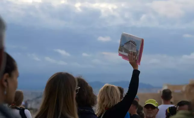 A tourist guide holds an illustration of the historical 5th century B.C. Parthenon temple as she speaks to a group atop the Acropolis hill in Athens, Friday, Oct. 31, 2025. (AP Photo/Petros Giannakouris)