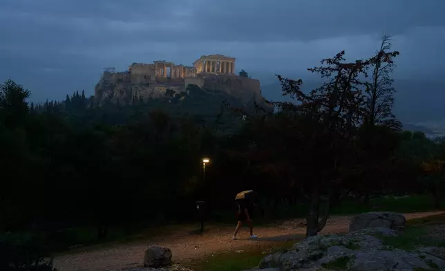 A woman walks with her umbrella during a rainfall at Pnyx below the Parthenon temple on Acropolis hill in Athens, Monday, Oct. 20, 2025. (AP Photo/Petros Giannakouris)