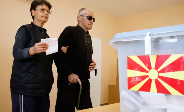 A woman holding ballots helps a man with impaired vision walk to the ballot boxes during the runoff local elections, at a polling station in Skopje, North Macedonia, on Sunday, Nov. 2, 2025. (AP Photo/Boris Grdanoski)
